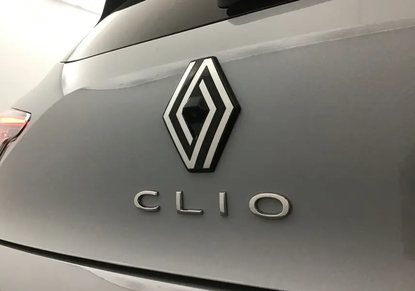 Gros plan sur le logo Renault avec caméra intégrée et le nom Clio sur la malle arrière gris Rafale.