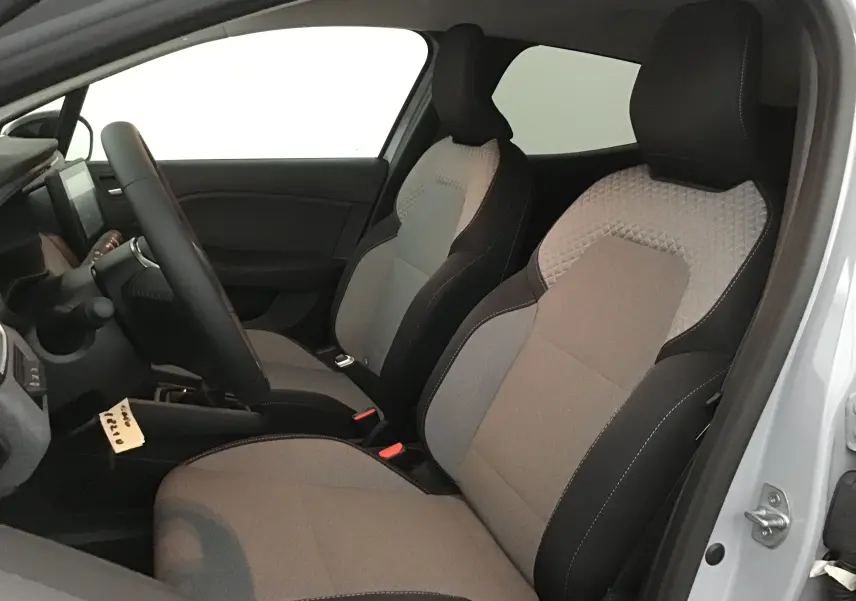 Vue intérieure côté conducteur de la Renault Clio V 2025, sièges tissu gris clair et noir avec surpiqûres contrastées.