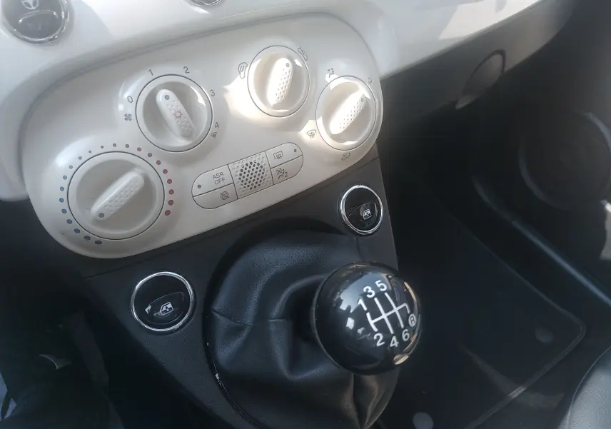 Gros plan sur la console centrale blanche et le levier de vitesses manuel noir d'une Fiat 500 blanche, version hybride.