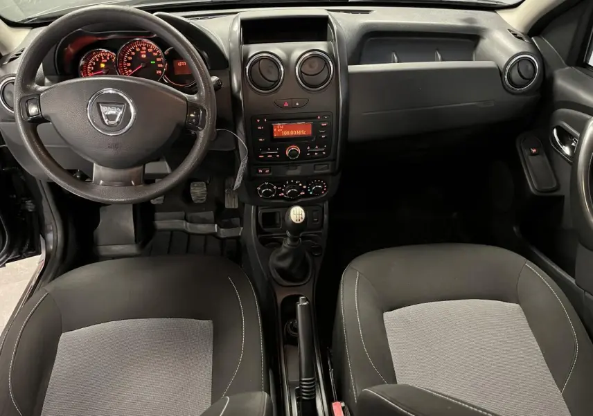 Vue intérieure avant du Dacia Duster noir 2016, volant, tableau de bord et sièges bicolores gris et noir visibles.