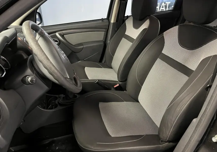 Intérieur avant droit du Dacia Duster 2016, sièges bicolores gris et noir avec volant et levier de vitesse visibles.