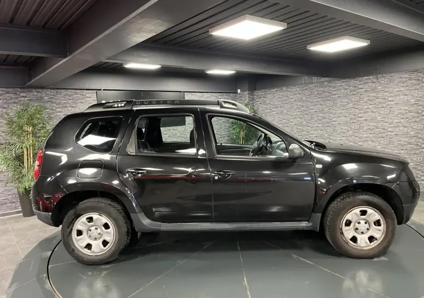 Profil côté gauche d'un Dacia Duster noir 2016 avec barres de toit et jantes acier 16 pouces en intérieur.