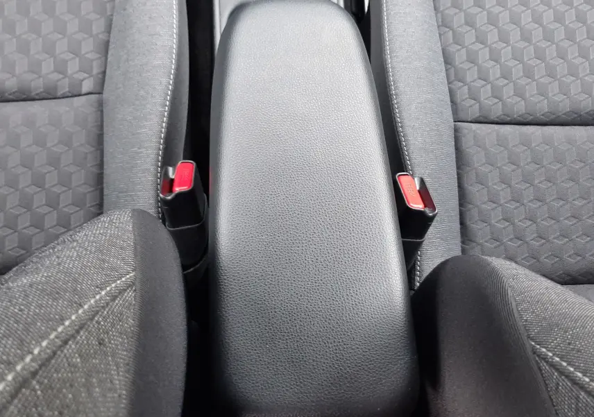 Vue plongeante sur l'accoudoir central noir et les sièges tissu gris de la Toyota Yaris 1.5 Hybrid 2023.