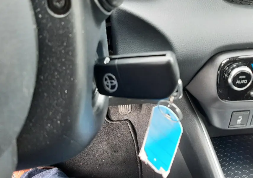 Gros plan intérieur sur la clé Toyota insérée dans le contact, avec tableau de bord et pédales visibles en arrière-plan.