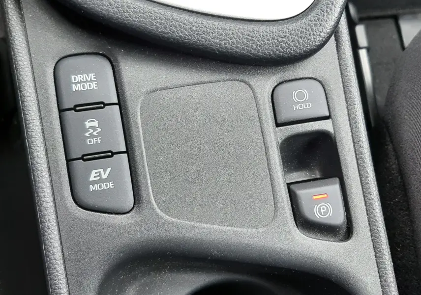Vue rapprochée de la console centrale noire de la Toyota Yaris 1.5 Hybrid 2023, avec boutons Drive Mode, EV Mode et frein à main électronique.