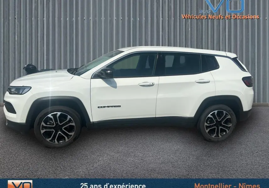 Profil côté gauche du Jeep Compass blanc 2024 avec jantes 17 pouces et roue de secours visible sur fond industriel.