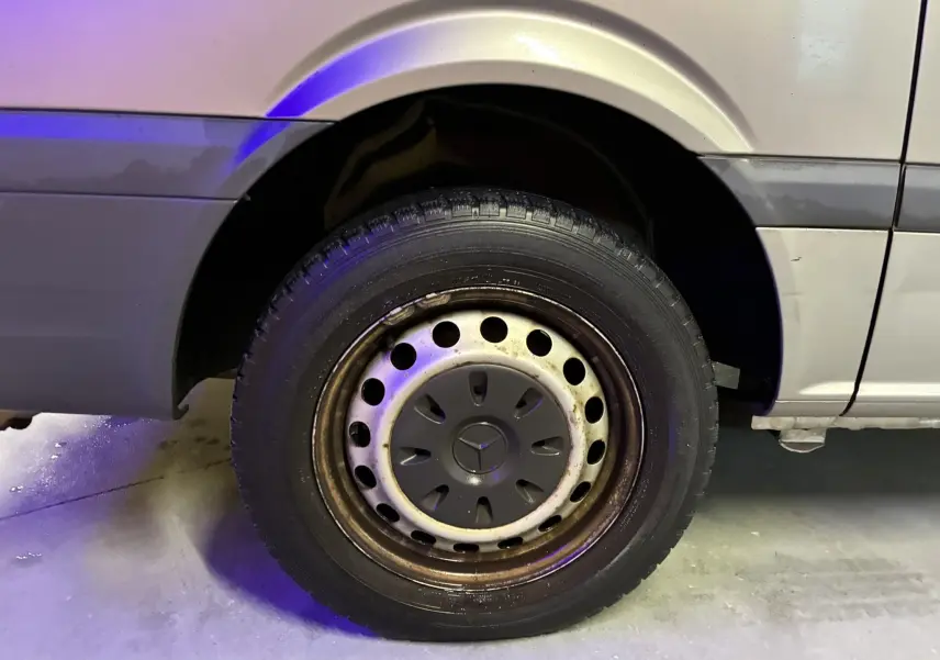 Gros plan sur la roue arrière droite d’un Mercedes Vito gris 2012, montrant la jante acier perforée et le passage de roue.