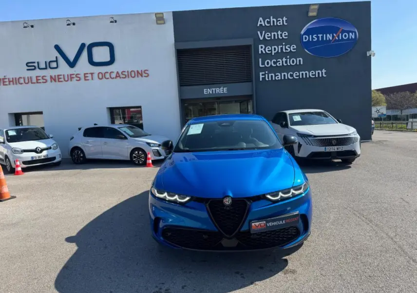 Vue avant d'un Alfa Romeo Tonale bleu foncé 2025, avec calandre caractéristique et phares LED allumés, devant un concessionnaire.