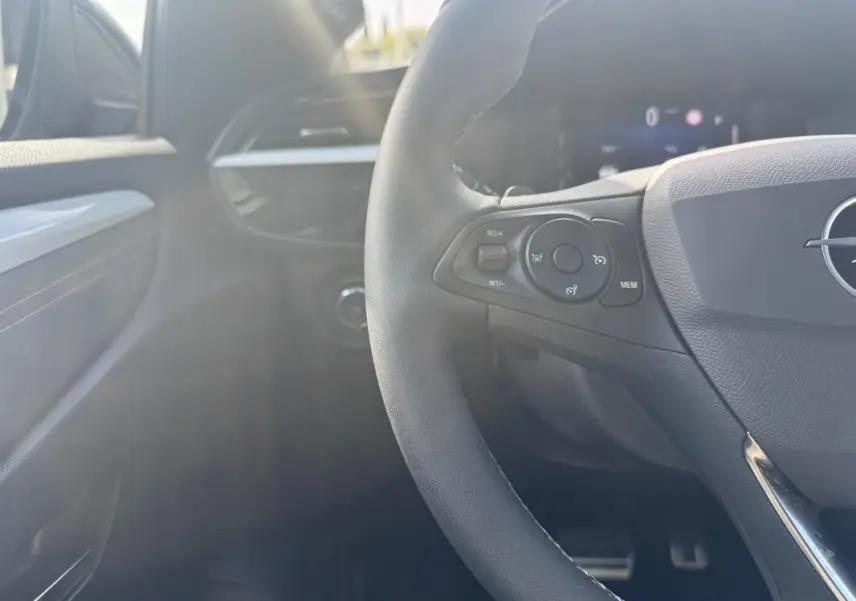 Vue intérieure côté gauche du volant noir d'une Opel Corsa 2025, avec commandes au volant et tableau de bord partiellement visible.
