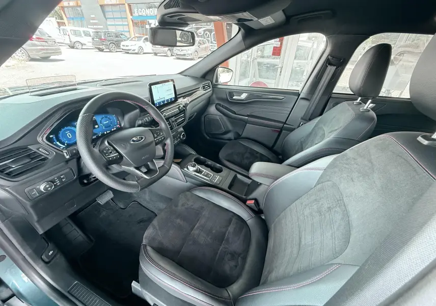 Intérieur avant droit du Ford Kuga bleu azur 2023 avec sièges cuir et alcantara, volant ST-Line à surpiqûres rouges.
