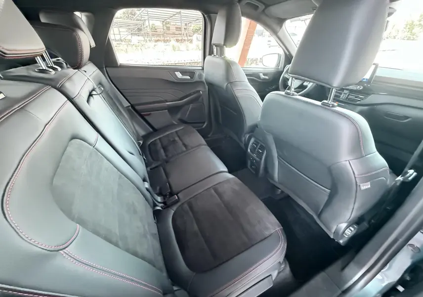 Vue intérieure arrière du Ford Kuga 2023 ST-Line X, sièges en cuir noir avec surpiqûres rouges et inserts alcantara.