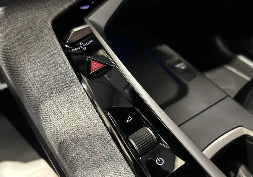 Gros plan sur la console centrale du Peugeot 5008 Hybrid 2025, montrant les boutons Drive Mode et warning sur finition noire brillante.