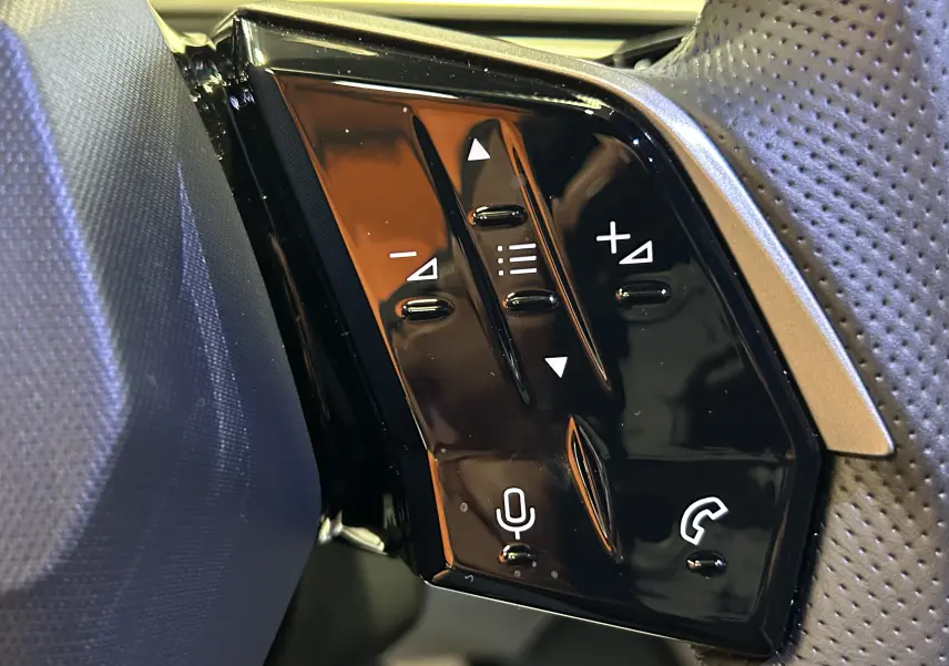 Gros plan sur les commandes noires du volant côté gauche du Peugeot 5008 Hybrid blanc, avec boutons volume et téléphone.