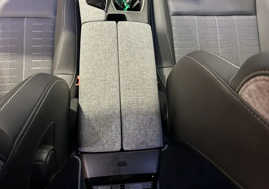 Vue plongeante sur la console centrale grise et les sièges en tissu et cuir noir de la Peugeot 5008 Hybrid 2025.