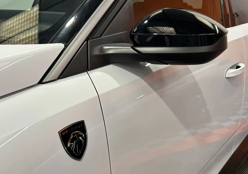 Gros plan sur le côté gauche blanc du Peugeot 5008 Hybrid avec rétroviseur noir brillant et logo lion distinctif.