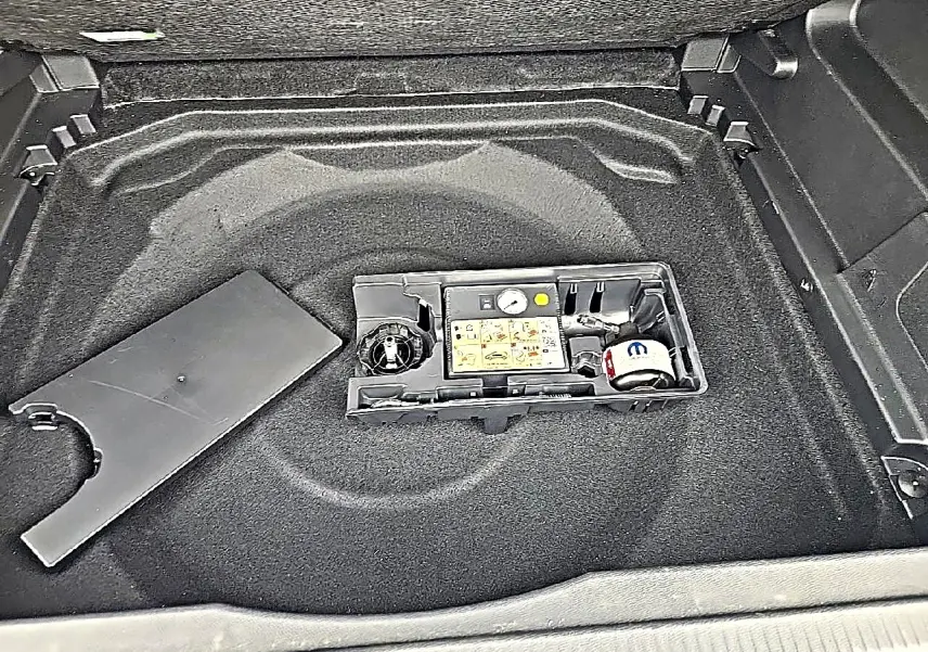 Vue plongeante sur le coffre du Citroën C5 Aircross gris, montrant le rangement sous plancher avec kit de réparation pneus.