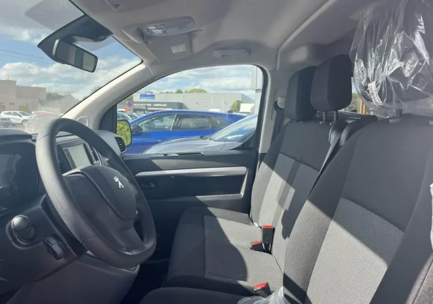 Vue intérieure côté conducteur du Peugeot Expert Fourgon 2023, sièges tissu gris et volant avec logo lion visible.