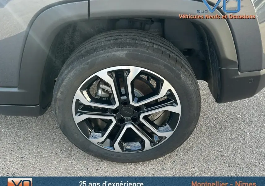 Gros plan sur la roue avant droite du Jeep Compass gris 2024 avec jante alliage bicolore et logo Jeep au centre.