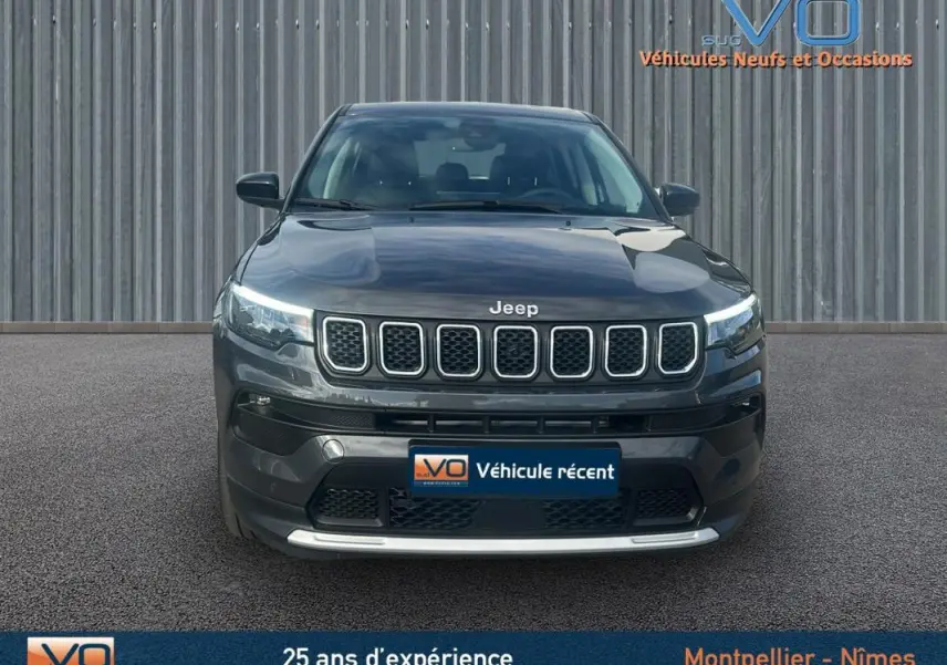 Vue frontale d'un Jeep Compass gris 2024 avec calandre distinctive et phares LED allumés sur fond industriel.
