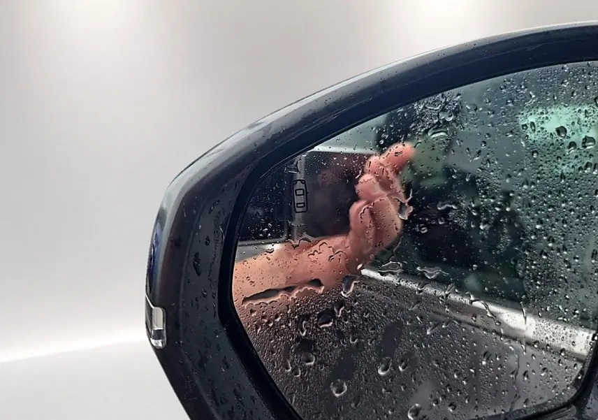 Rétroviseur droit gris du Citroën C5 Aircross 2025 avec gouttes d'eau et reflet flou d'une main.