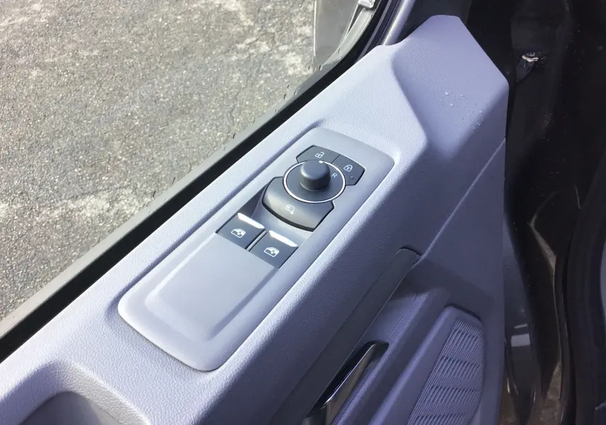 Gros plan sur la commande des vitres et rétroviseurs côté gauche de la porte d'un Volkswagen Transporter ProCab gris anthracite 2025.