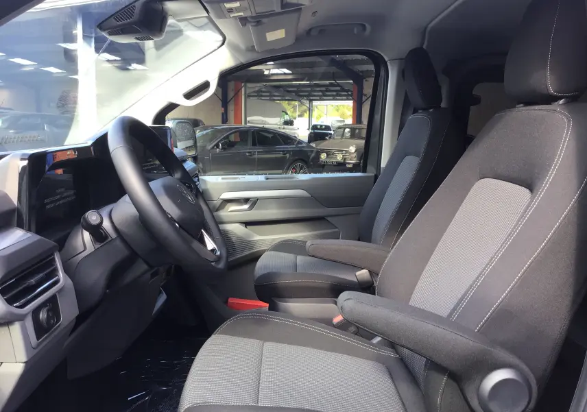 Intérieur avant du Volkswagen Transporter ProCab 2025 gris anthracite, sièges tissu gris avec accoudoirs et tableau de bord moderne.