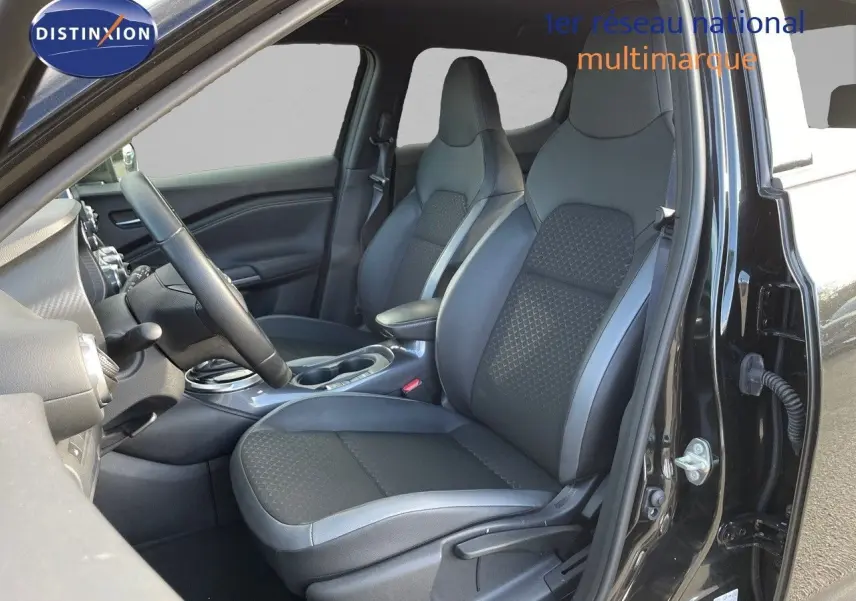 Intérieur avant droit du Nissan Juke 2024 noir métal, sièges en cuir gris et tableau de bord visible.