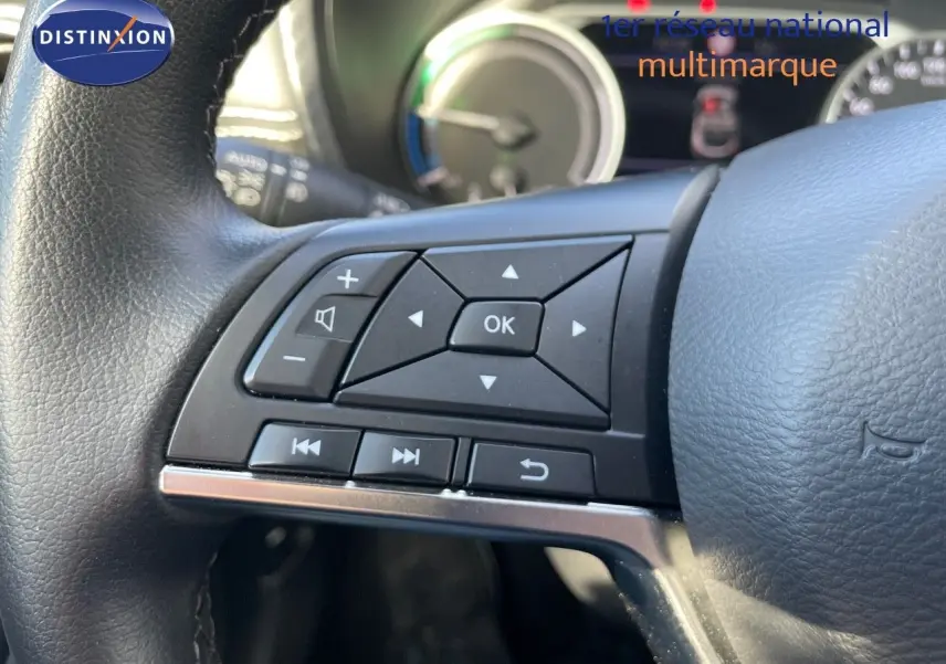 Gros plan sur les commandes multifonctions à gauche du volant noir du Nissan Juke 2024 hybride, tableau de bord en arrière-plan.