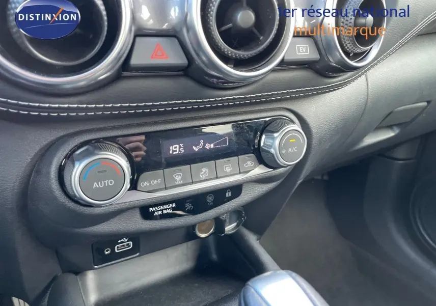 Console centrale du Nissan Juke 2024 en noir métal, vue rapprochée du tableau de bord avec commandes climatisation et prise USB.