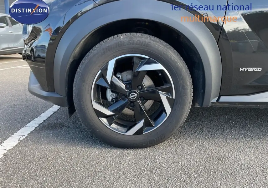 Gros plan sur la roue avant gauche noire métallisée du Nissan Juke 2024 hybride avec jante biton et logo Nissan visible.