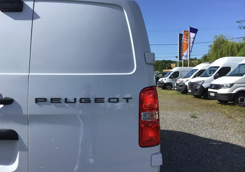 Vue arrière droite d'un Peugeot Expert Fourgon blanc avec feux rouges, sur un parking de véhicules utilitaires.
