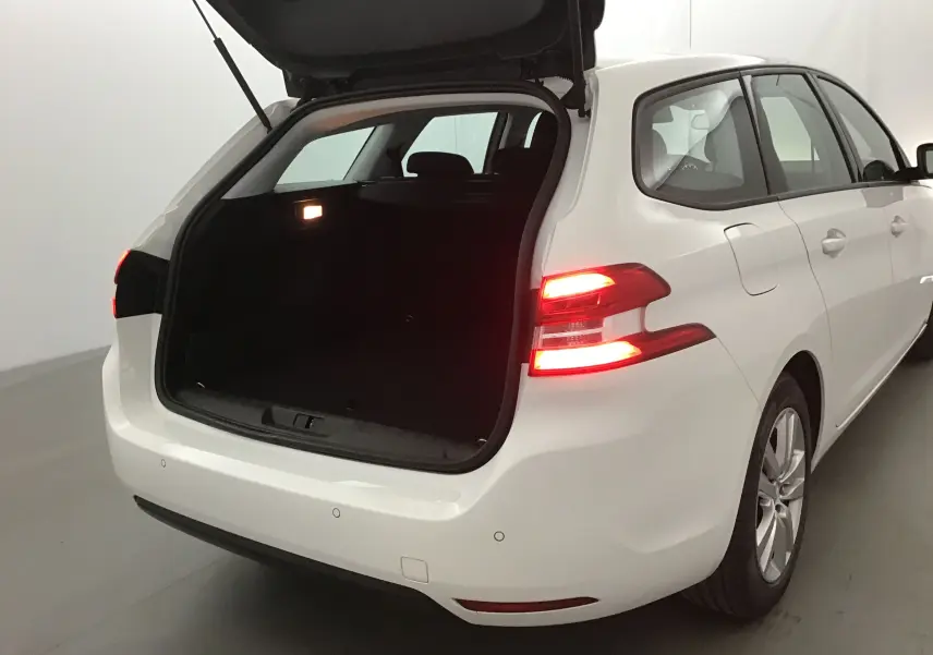 Peugeot 308 SW blanche vue 3/4 arrière droit avec coffre ouvert et feux arrière allumés dans un studio.
