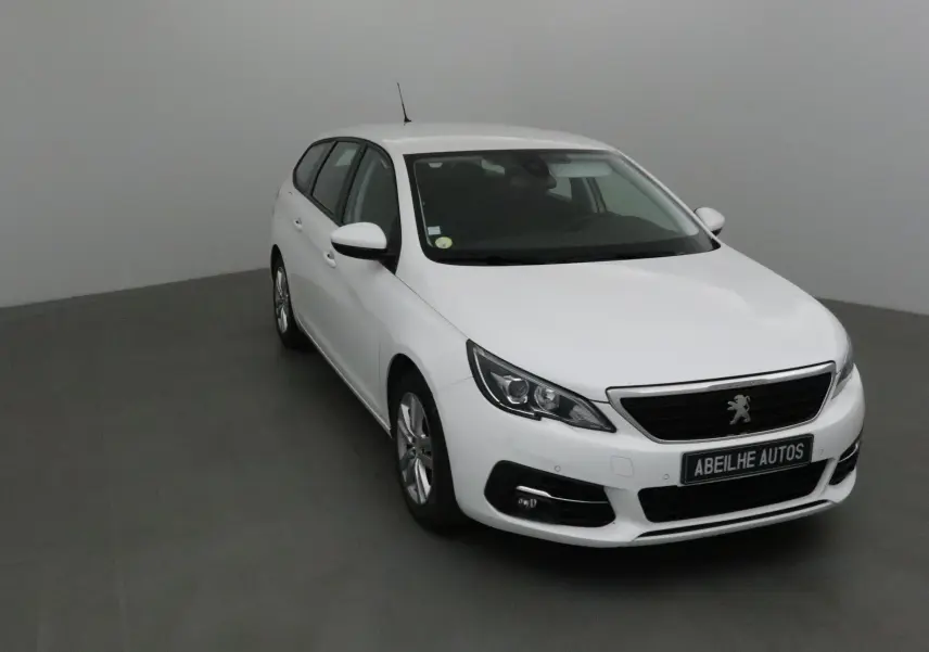 Peugeot 308 SW blanche vue en 3/4 avant droit dans un studio, avec calandre noire et jantes alliage.