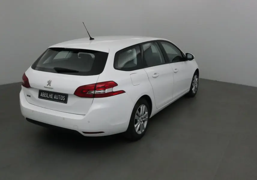 Peugeot 308 SW blanche vue 3/4 arrière droit dans un intérieur neutre avec feux arrière rouges distinctifs.