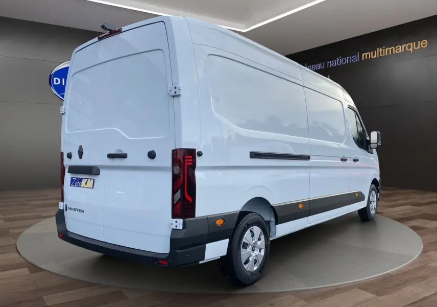 Vue 3/4 arrière droite du Renault Master blanc avec portes arrière tôlées et enjoliveurs noirs sur fond intérieur showroom.