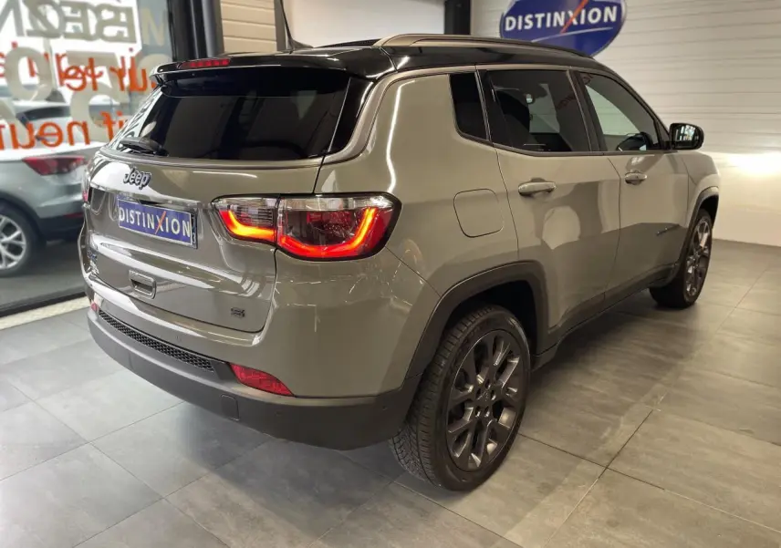 Vue 3/4 arrière droit du Jeep Compass gris foncé avec feux arrière allumés et jantes alliage en showroom.