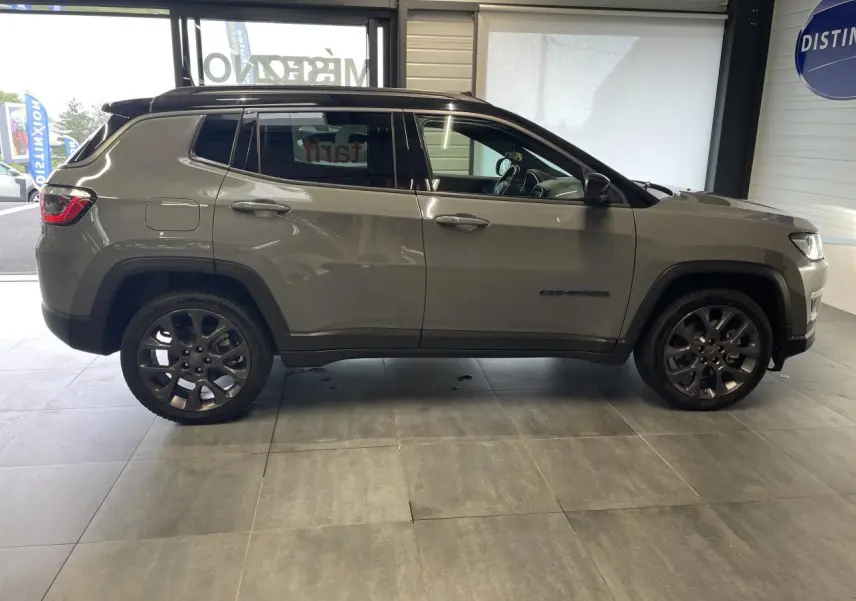 Profil côté gauche d'un Jeep Compass gris foncé avec jantes alliage et toit noir en intérieur showroom.