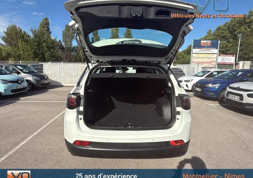 Vue arrière ouverte du Jeep Compass blanc 2024 montrant le coffre spacieux dans un parking extérieur.