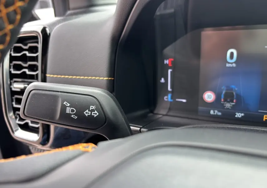 Gros plan sur le commodo de clignotants et tableau de bord numérique du Ford Ranger Wildtrak Plus noir agate, intérieur avec surpiqûres orange.