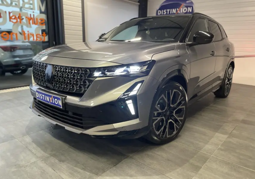 Renault Austral gris métallisé en 3/4 avant droit, avec calandre noire et jantes alliage 20 pouces distinctives.