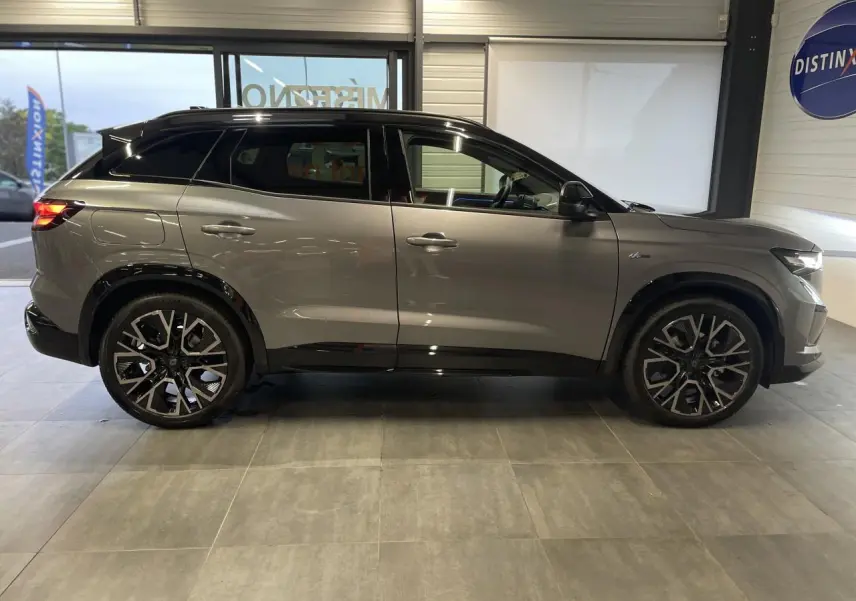 Profil droit d'un Renault Austral gris métallisé avec toit noir étoilé et jantes alliage noires en showroom.