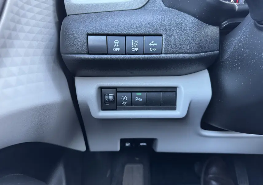 Vue rapprochée des commandes situées sous le volant côté gauche d'une Suzuki Swift 2024 blanc/gris hybride.