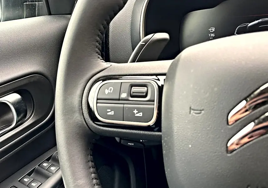 Gros plan sur le volant noir du Citroën C5 Aircross 2025 avec commandes multifonctions côté gauche et porte intérieure visible.