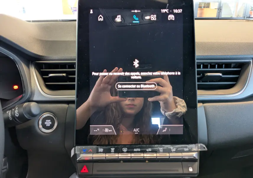 Écran tactile central du tableau de bord du Renault Captur E-Tech 2025 avec commandes climatisation et bouton start/stop visible.