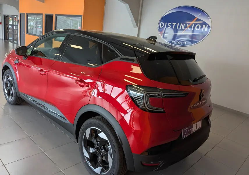Renault Captur E-Tech hybride 2025 rouge flamme toit noir, vue 3/4 arrière droit en showroom intérieur.
