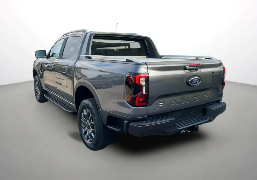 Ford Ranger 3.0 V6 Wildtrak Plus gris carbone vu 3/4 arrière droit avec benne et barres de toit visibles.