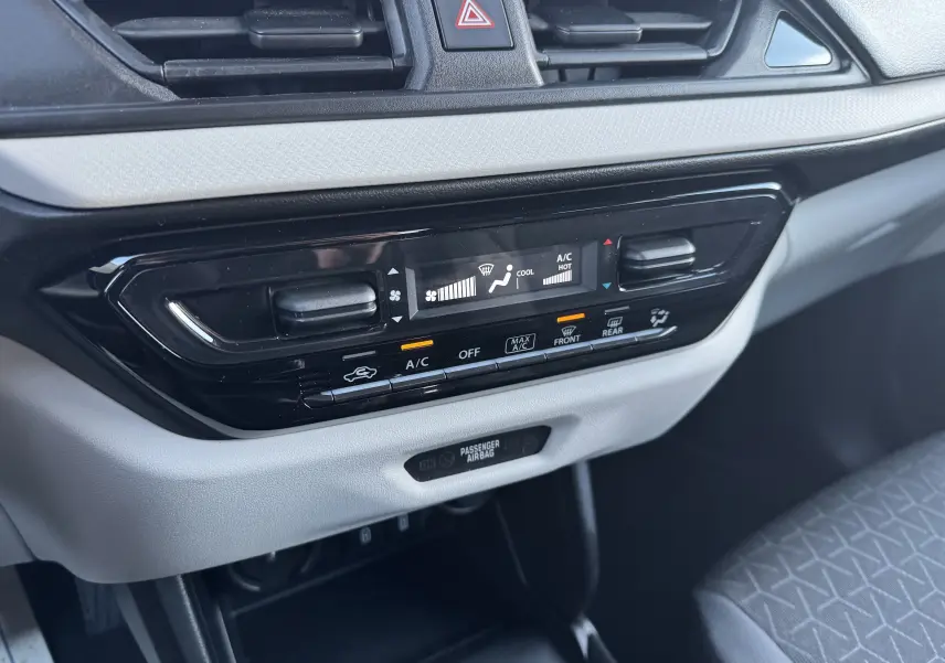 Gros plan sur la console centrale de la Suzuki Swift blanche 2025, montrant les commandes de climatisation et l'airbag passager.