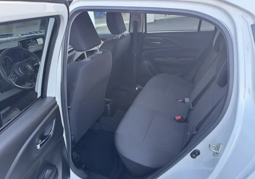 Intérieur arrière de la Suzuki Swift blanche 2025, vue côté gauche montrant les sièges arrière en tissu noir et la portière ouverte.