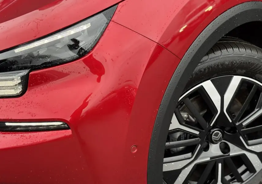 Gros plan sur l'avant droit rouge Elixir d'une Citroën C4 Hybrid 2025, avec phare LED et jante alliage 18 pouces.