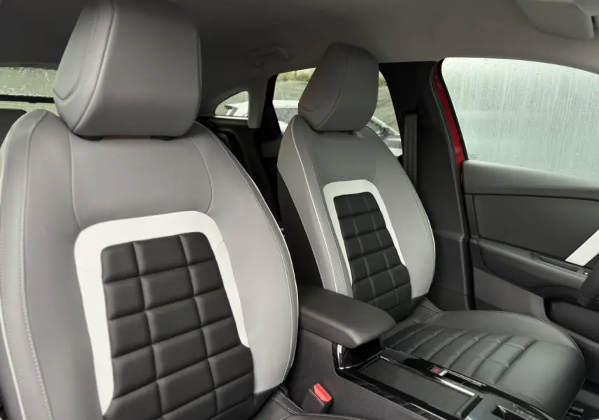 Vue intérieure des sièges avant gris clair et noir de la Citroën C4 Hybrid 2025 avec accoudoir central et porte-gobelets.
